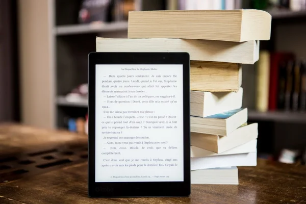 Livros físicos empilhados ao lado de um leitor digital