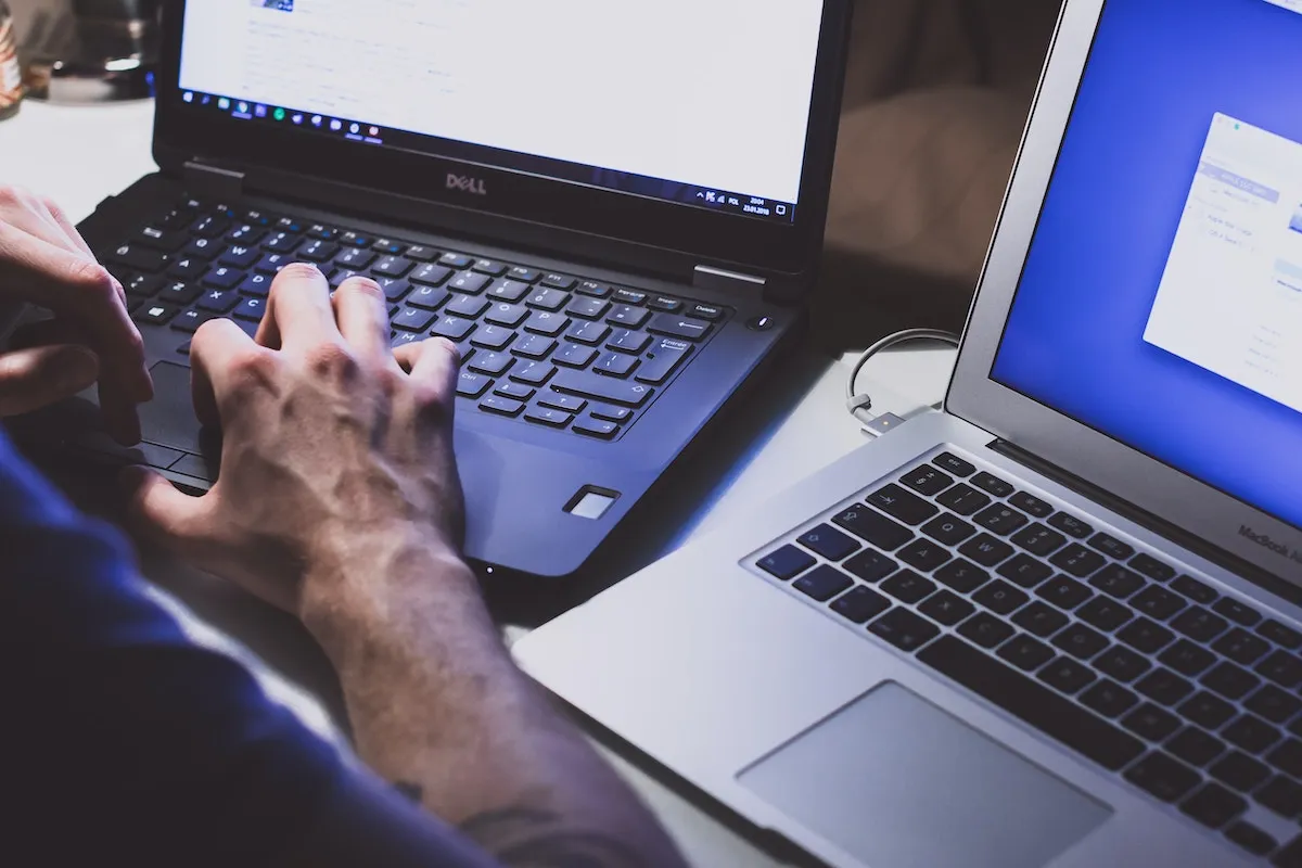 Um home digitando em dois laptops ao mesmo tempo